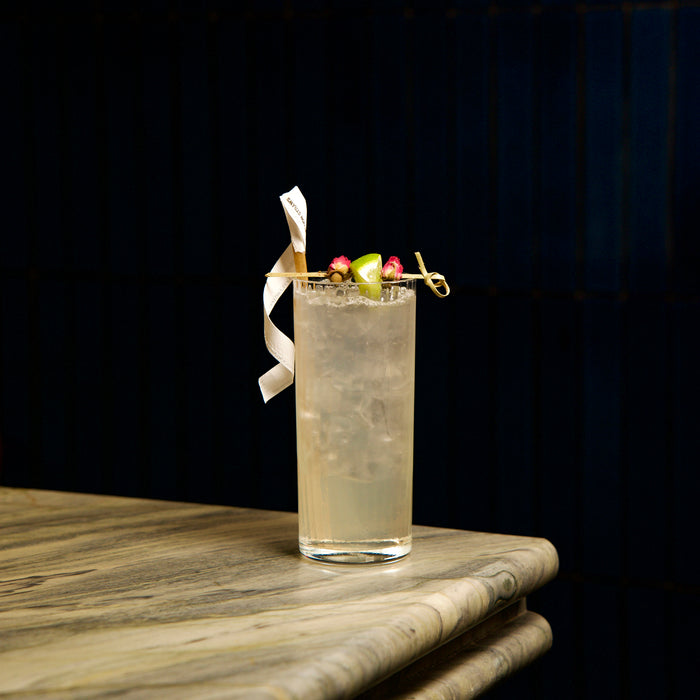 Cocktail in Exclusive Tom Collins glass with colorful garnish on a marble surface against a dark background